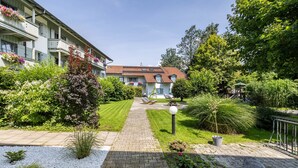 Een binnentuin met een geplaveid pad, een klein tuinpartij met planten en een rots, en een gebouw met balkons.