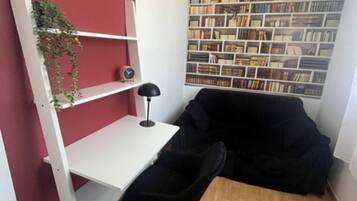 A compact room with a white desk, a black chair, a bookshelf, and a red accent wall.
