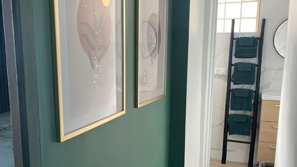 Un couloir aux murs de couleur turquoise, orné de deux œuvres d’art abstraites encadrées, et doté d’un plancher en bois.