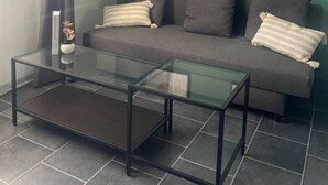 Un salon moderne avec une table basse en verre, un canapé gris et deux œuvres d’art encadrées accrochées au mur.