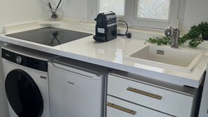 Une cuisine compacte dotée d’un lave-linge et d’un sèche-linge intégrés, d’un plan de travail avec une machine à café et d’une fenêtre ornée de vitraux décoratifs.