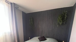 Une chambre à coucher avec un lit, une table de chevet, une plante et une fenêtre avec des rideaux.