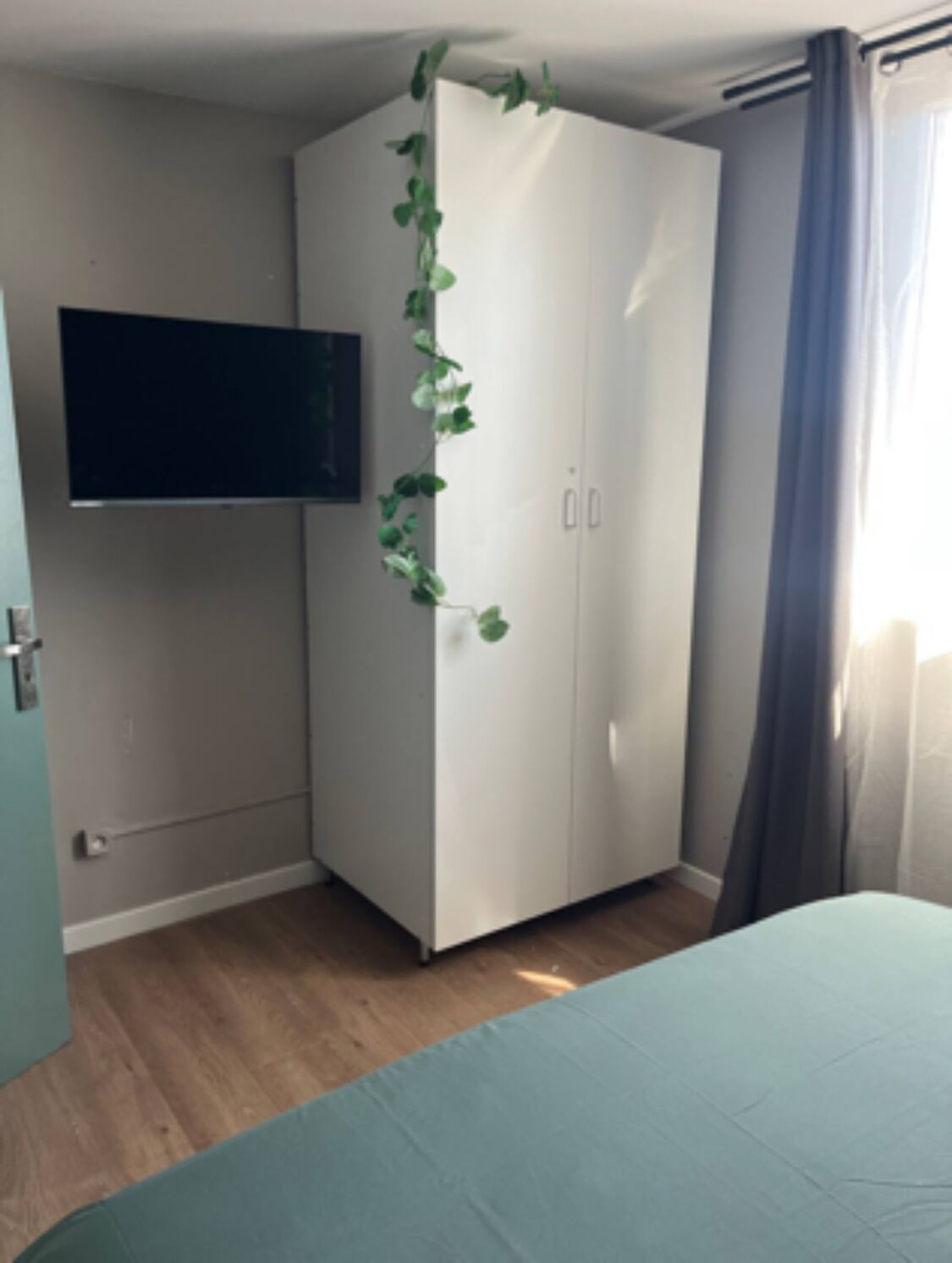 Een slaapkamer met een bed, een kledingkast, een flatscreen-tv en een raam met gordijnen.