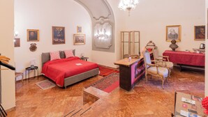 A hotel room with a bed, a desk, a chair, a chandelier, and framed pictures on the walls. - Palazzo del Bono suites (Palermo)