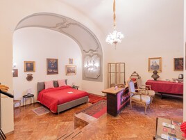 A hotel room with a bed, a desk, a chair, a chandelier, and framed pictures on the walls.