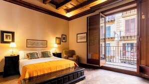 A hotel room with a bed, a chair, a nightstand, and a window with a view of buildings. - Palazzo del Bono suites (Palermo)