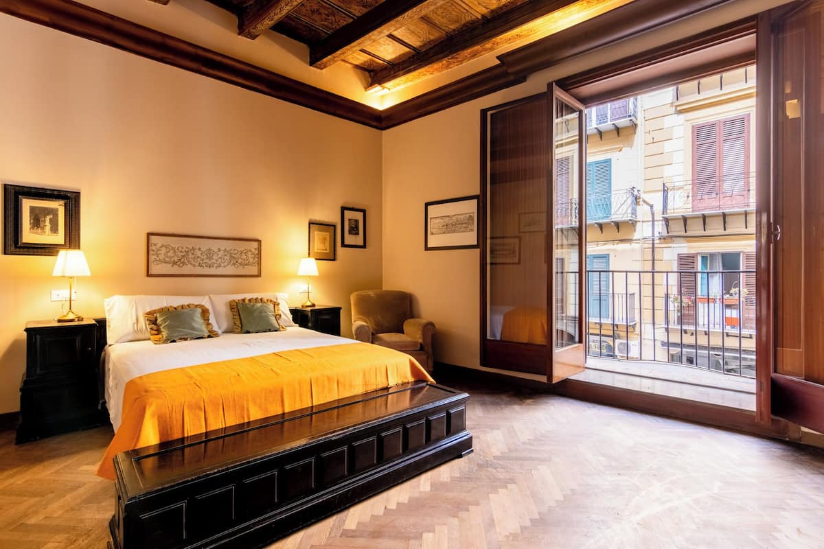 A hotel room with a bed, a chair, a nightstand, and a window with a view of buildings.