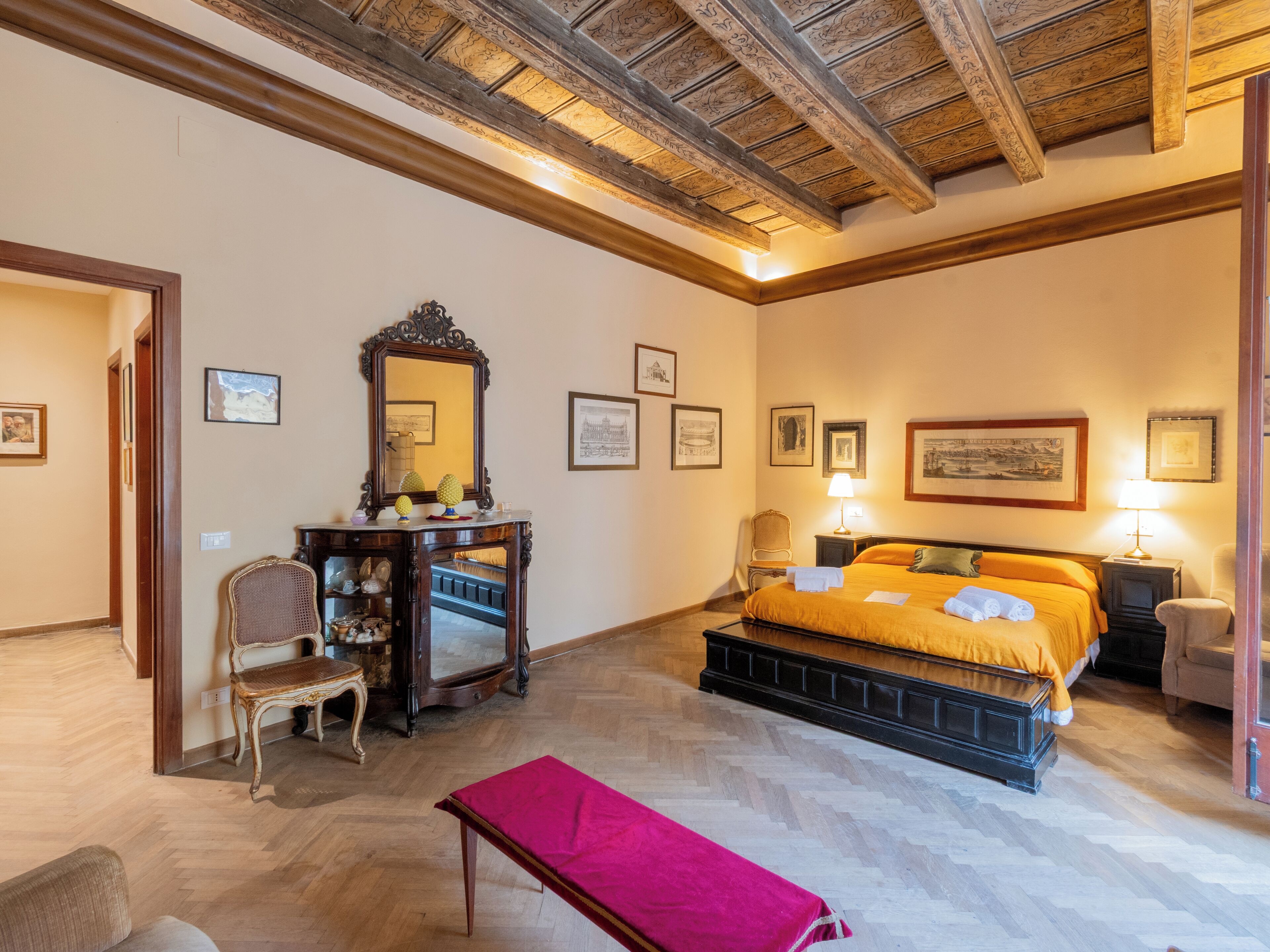A bedroom with a wooden ceiling, a bed with an orange bedspread, a wooden dresser, a chair, and a bench.