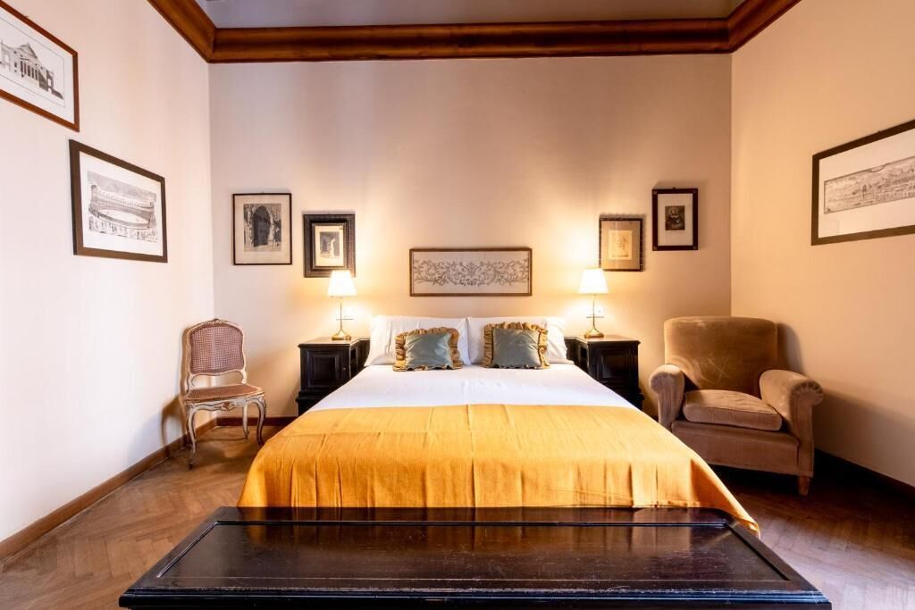 A hotel room with a large bed, two nightstands, two lamps, a chair, and framed pictures on the walls.