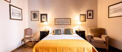 A hotel room with a large bed, two nightstands, two lamps, a chair, and framed pictures on the walls.