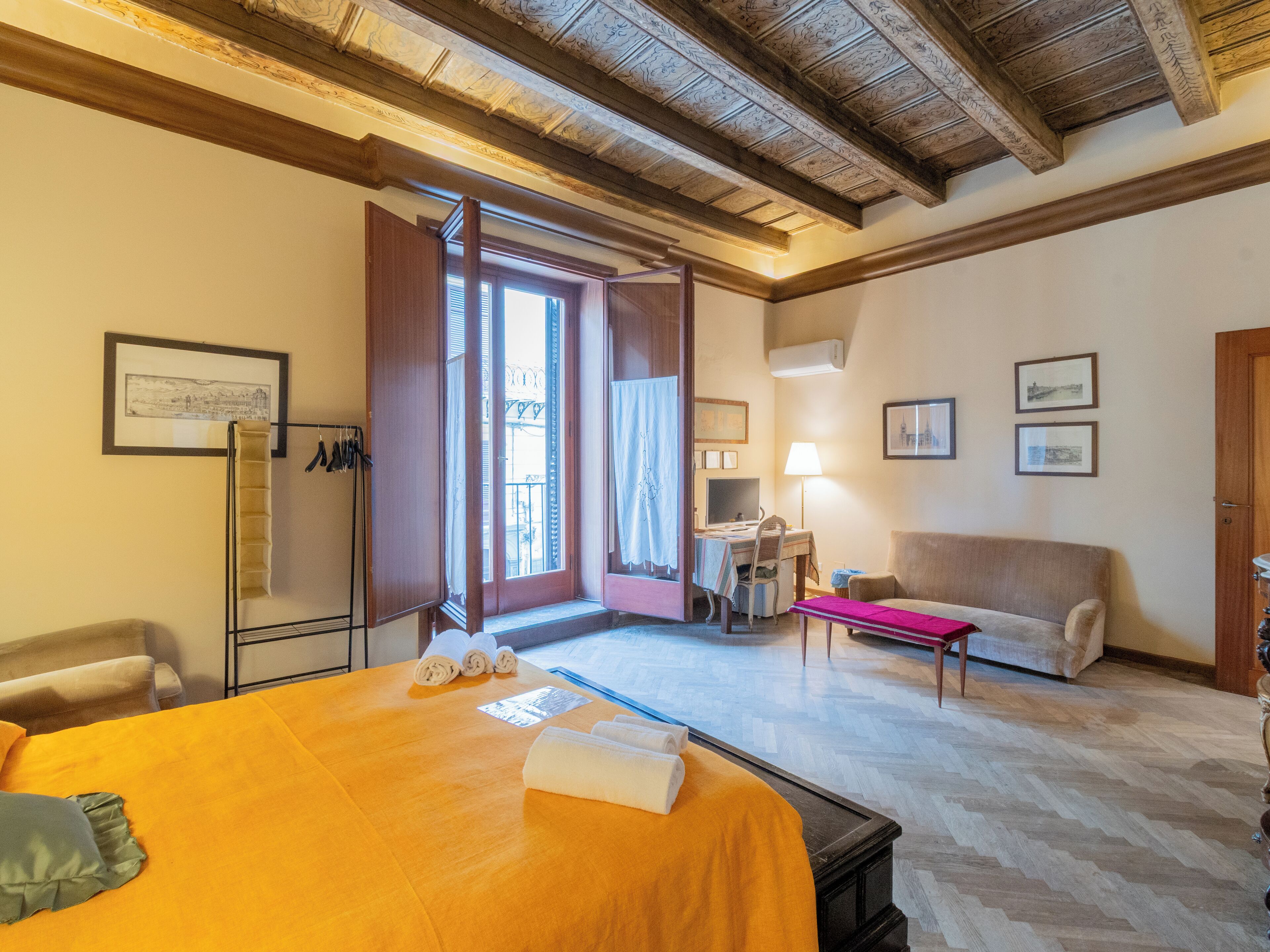 A hotel room with a bed, a desk, a chair, a sofa, and a balcony with a view.
