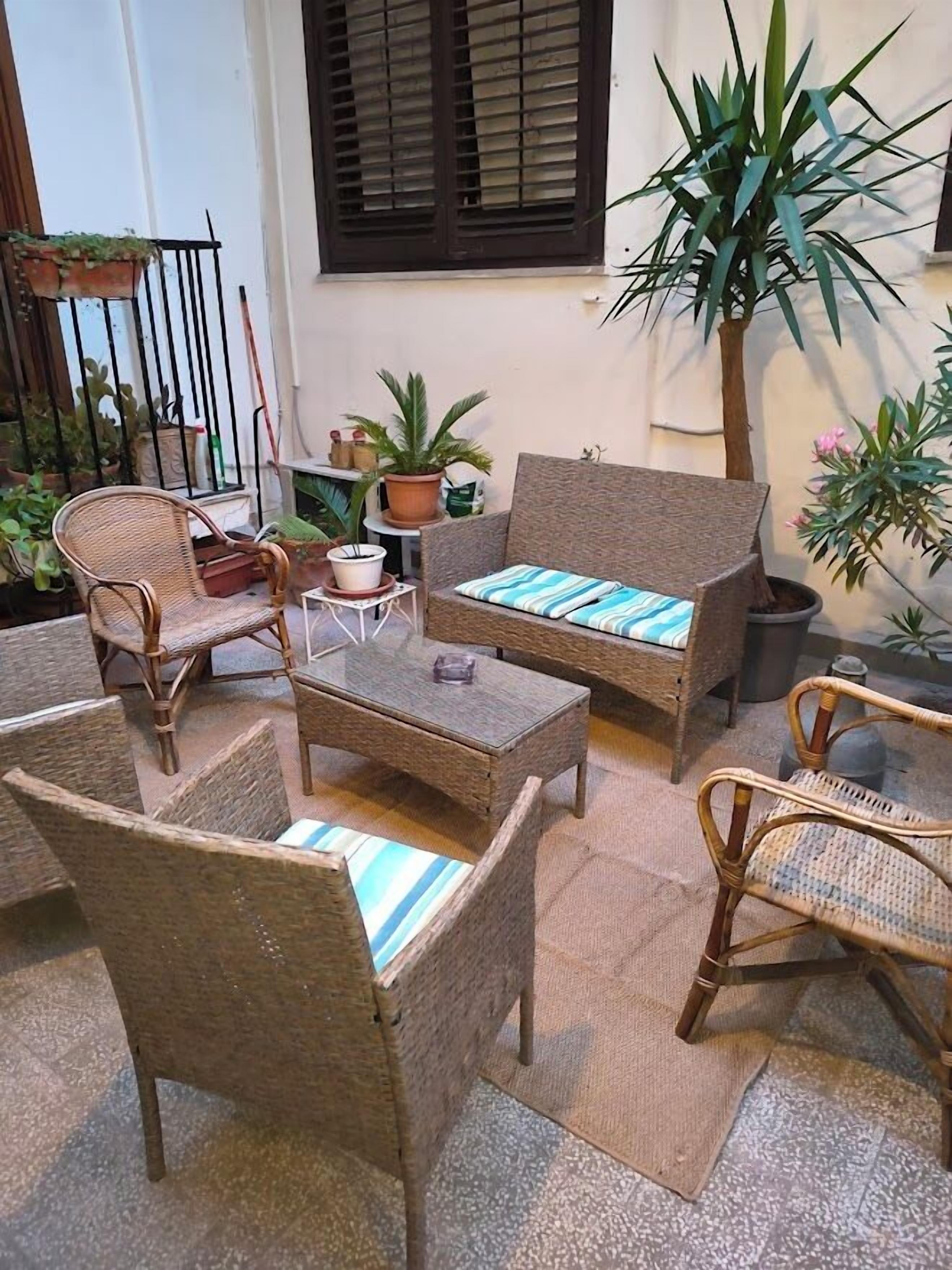 Ein Patio mit Korbmöbeln, darunter eine Couch und Stühle, ein kleiner Tisch und Blumentöpfe.