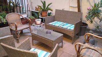 Ein Patio mit Korbmöbeln, darunter eine Couch und Stühle, ein kleiner Tisch und Blumentöpfe.