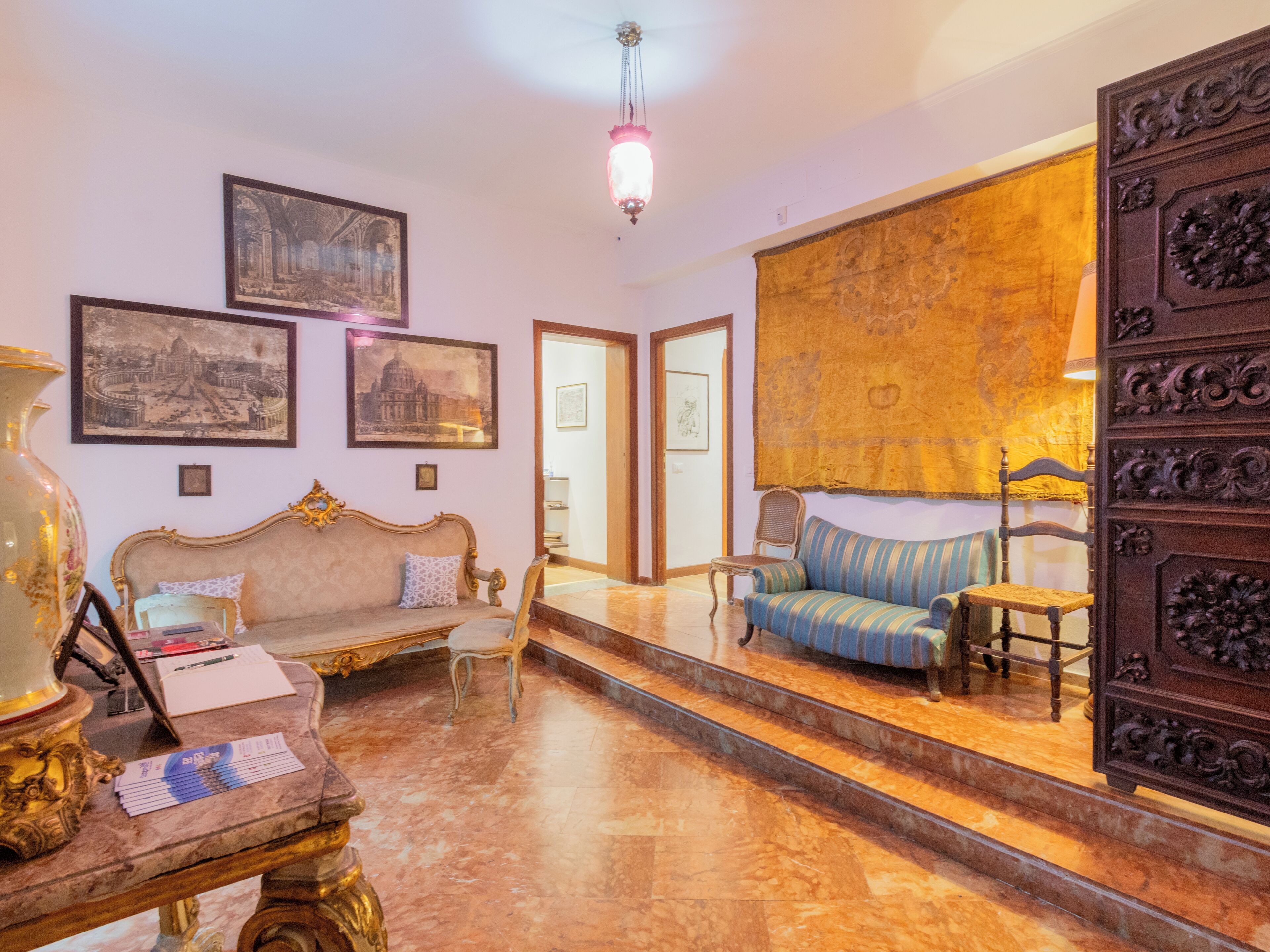 Una habitación con piso de mármol, un sofá, una silla, una mesa con papeles y cuadros en la pared.