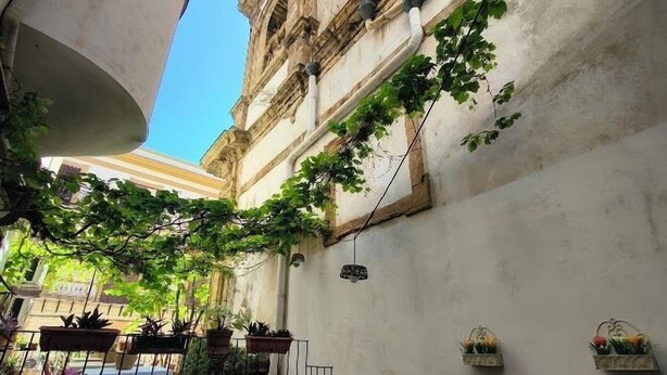 A courtyard with a view of a historic building, outdoor seating with wicker chairs, and potted plants. - Palazzo del Bono suites (Palermo)