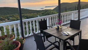 Une terrasse avec une table et des chaises, offrant une vue panoramique sur un paysage vallonné et un plan d’eau.