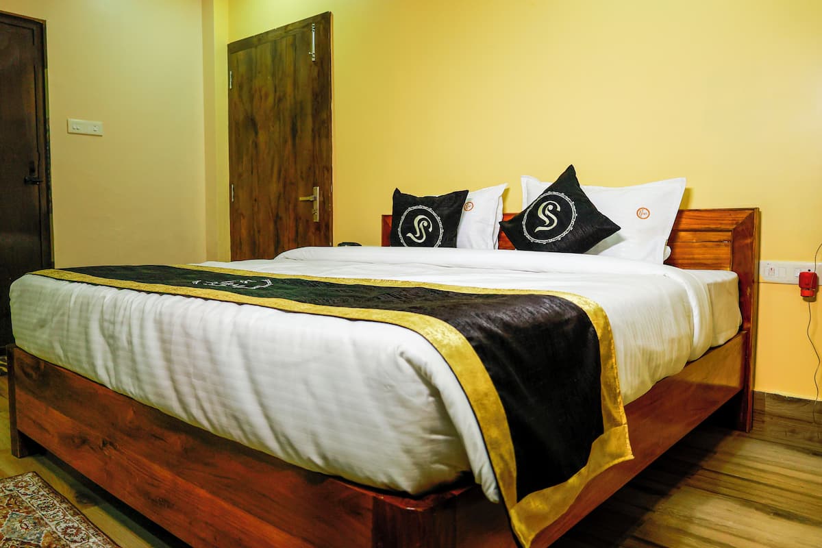 A bed with a wooden frame, white bedding, and black and white pillows with a logo.
