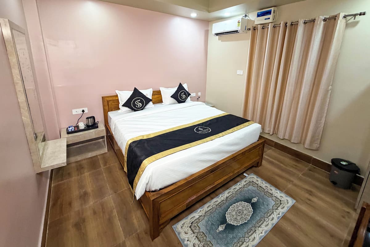 A neatly arranged bedroom with a wooden bed, a bedside table with a lamp, a wall-mounted air conditioner, and a window with curtains.