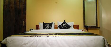 A neatly made bed with a wooden headboard, two pillows with a logo, a bedside table with a phone, and a mirror on the wall.