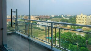 A balcony with a glass railing overlooking a residential area with various buildings and greenery. - Silicon Inn By Suviraj Hotels (Puri)