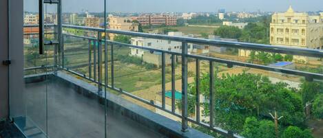 A balcony with a glass railing overlooking a residential area with various buildings and greenery.