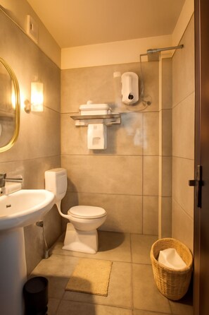 A bathroom with a sink, toilet, and shower. There is a basket and a mat on the floor. - Silicon Inn By Suviraj Hotels (Puri)