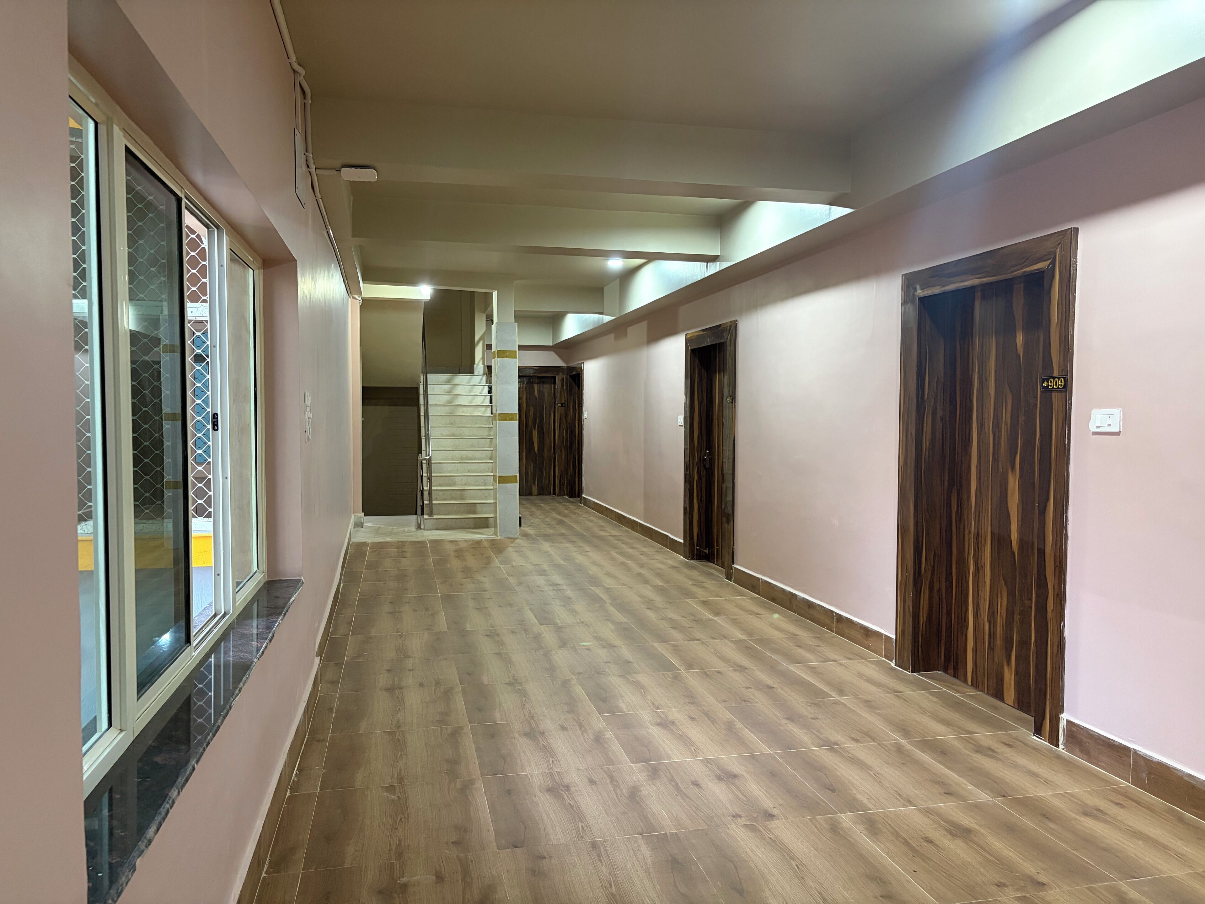 Un pasillo largo y estrecho con piso de madera, una escalera y varias puertas.