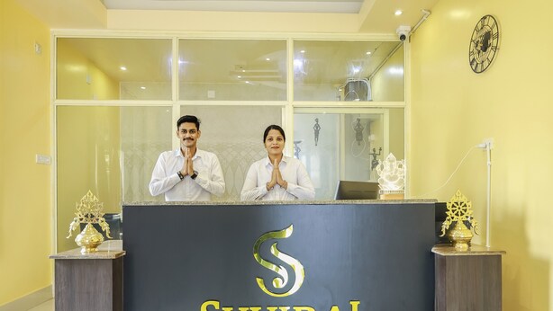 A reception desk with a logo and two individuals standing behind it. - Silicon Inn By Suviraj Hotels (Puri)