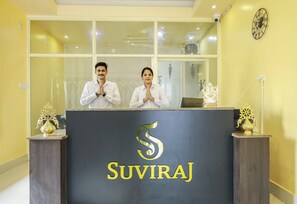 A reception desk with a logo and two individuals standing behind it. - Silicon Inn By Suviraj Hotels (Puri)