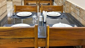 A dining area with wooden tables and chairs, arranged in a row. - Silicon Inn By Suviraj Hotels (Puri)