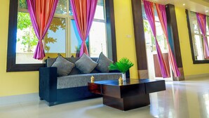 A modern hotel lobby with a sofa, a coffee table, and large windows with colorful curtains. - Silicon Inn By Suviraj Hotels (Puri)