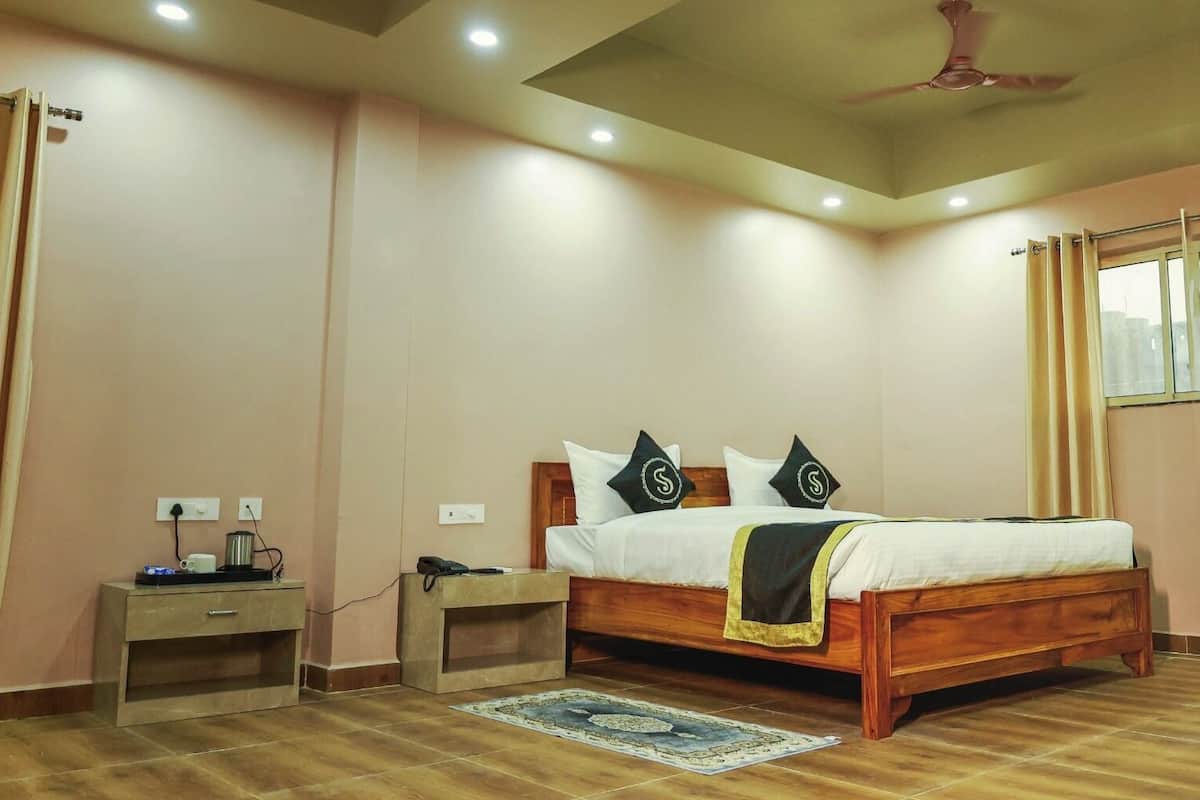 A bedroom with a wooden bed, two bedside tables, a nightstand, a ceiling fan, and a window with curtains.