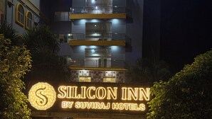The exterior of the Silicon Inn by Suviraj Hotels at night, featuring a multi-story building with illuminated signage and a gated entrance. - Silicon Inn By Suviraj Hotels (Puri)