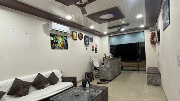 A modern living room with a sofa, coffee table, and a TV. There is a ceiling fan, a wall-mounted air conditioner, and a small plant on the coffee table. - Hotel Moti Palace (Shri Madhopur)