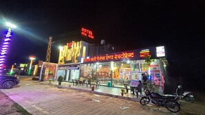 A brightly lit hotel with a neon sign, outdoor seating area, and a motorcycle parked in front. - Hotel Moti Palace (Shri Madhopur)