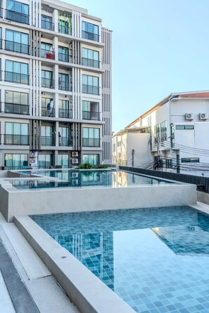 Ein modernes Gebäude mit Pool auf dem Dach, Balkonen und blauem Himmel.