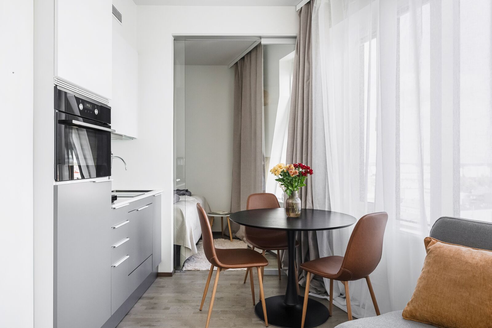 A modern kitchen with a built-in oven and a dining area with a round table and two chairs.