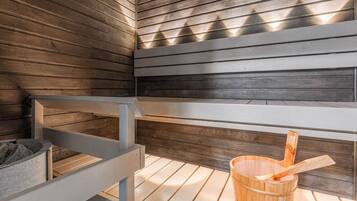 A sauna with wooden benches, a wooden bucket, and a stone container.