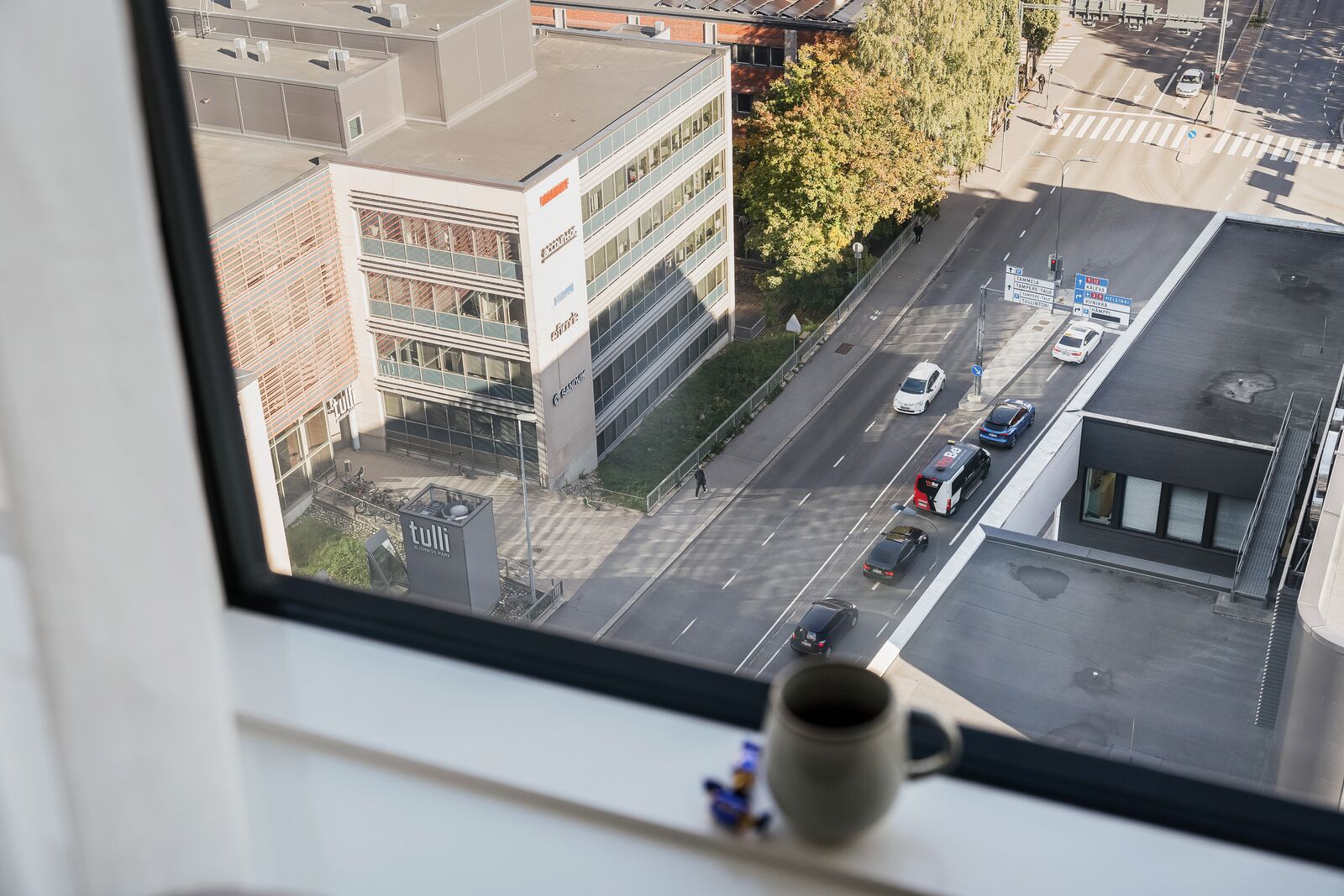 A view from a window overlooking a street with buildings, a crosswalk, and a few cars.
