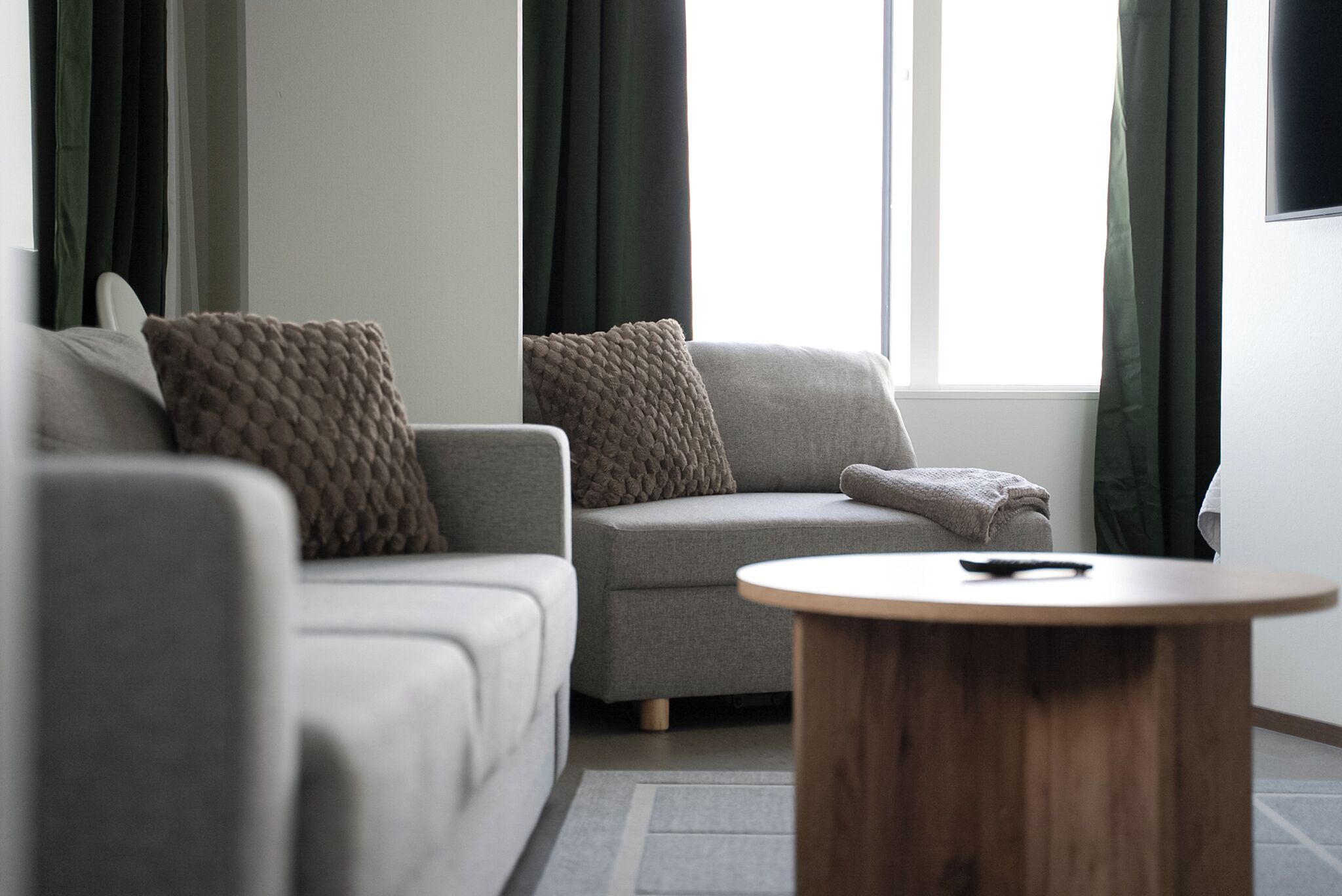 A modern living room with a grey sofa, a round wooden coffee table, and a window with curtains.