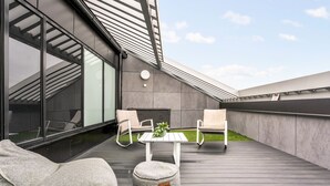 A modern outdoor patio with a wooden deck, two white chairs, a small round table, and a potted plant. - Topaasi - Nokia Arena by Come in (Tampere)