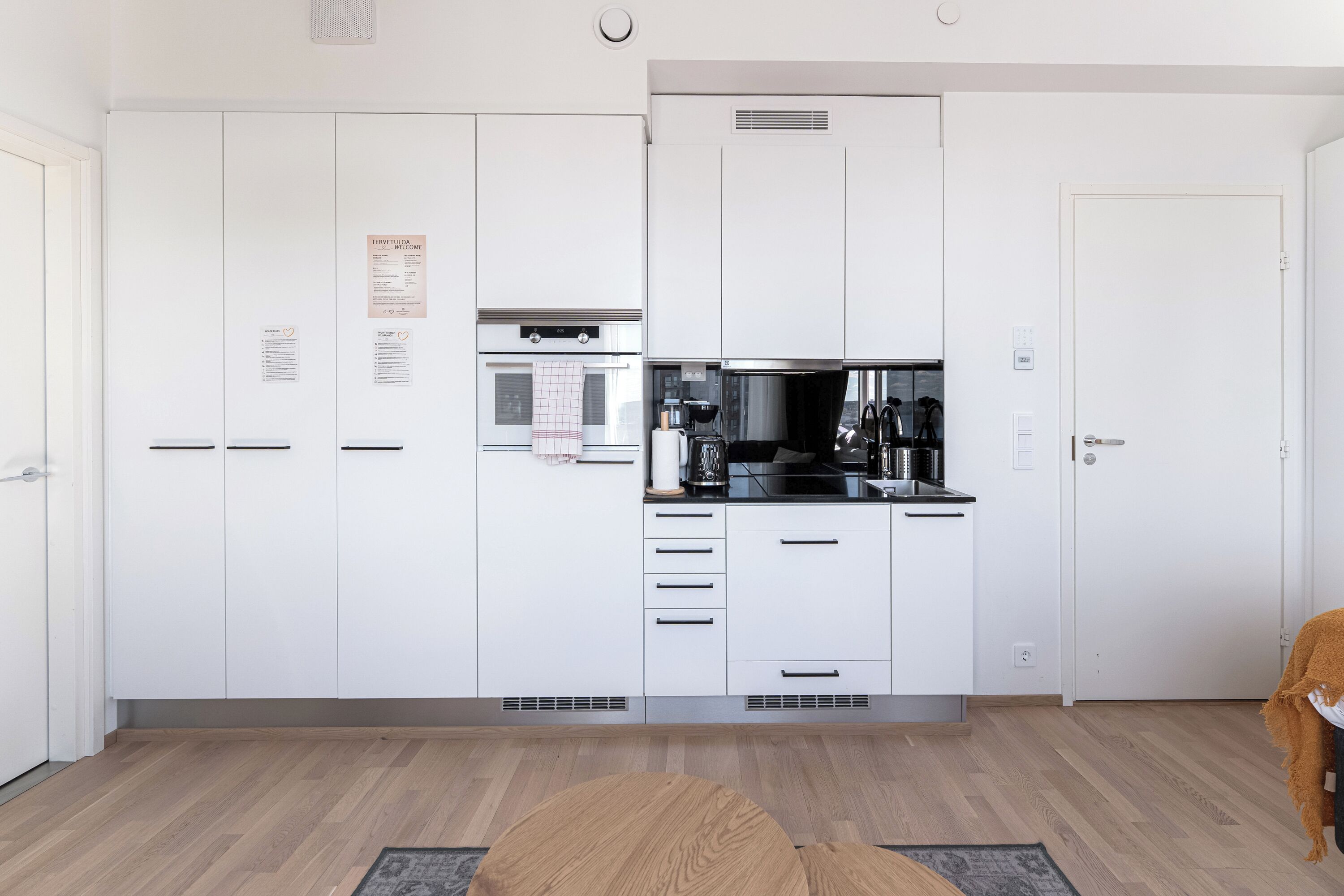 A modern kitchen with white cabinets, a built-in oven, and a coffee machine.