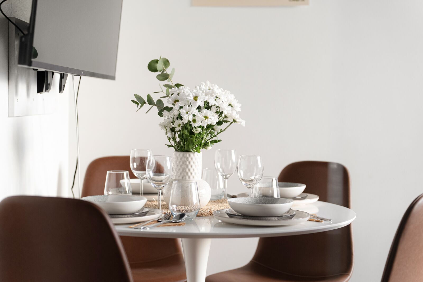 A dining table set with white plates, bowls, and glasses, surrounded by brown chairs.