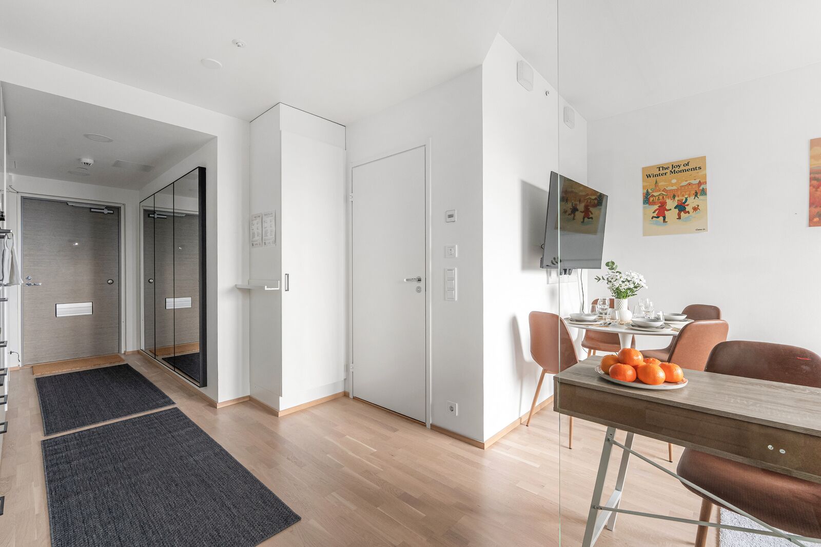 Un apartamento moderno con comedor, televisor montado en la pared y una puerta visible que da a otra habitación.