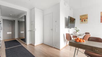 Un apartamento moderno con comedor, televisor montado en la pared y una puerta visible que da a otra habitación.