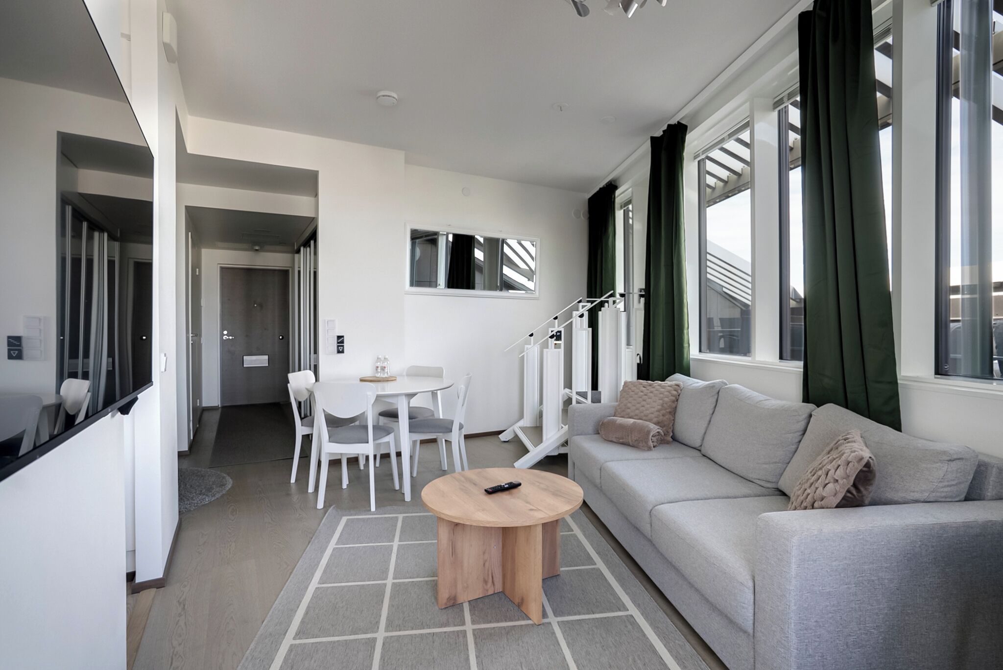 A modern living room with a sofa, a coffee table, a dining area with chairs, and a staircase.