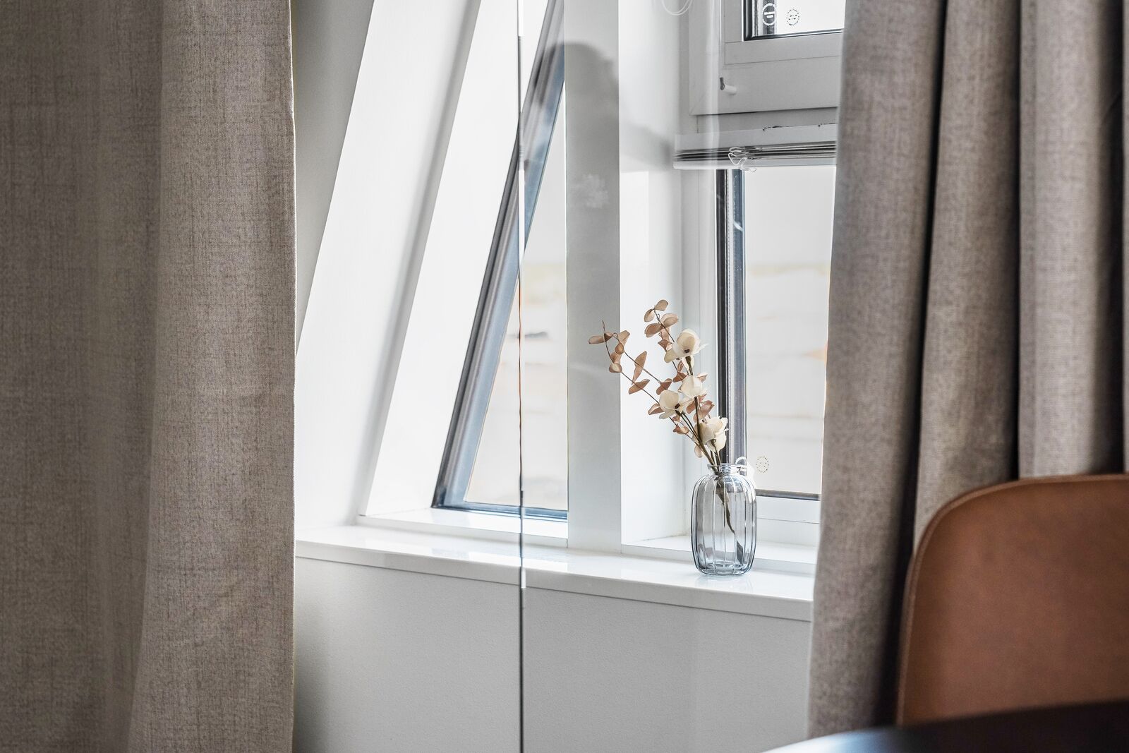 A room with a skylight, a vase with dried flowers, and a window with curtains.