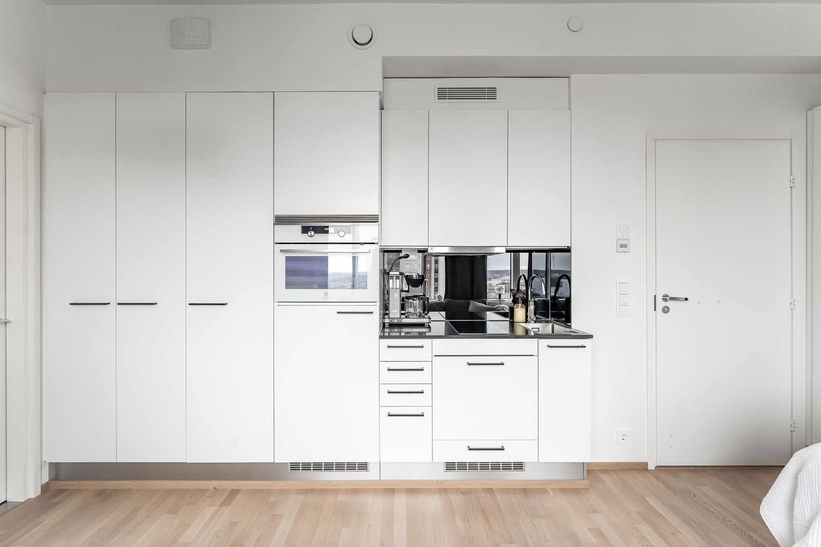 A modern kitchen with white cabinetry, a built-in oven, and a stainless steel sink.