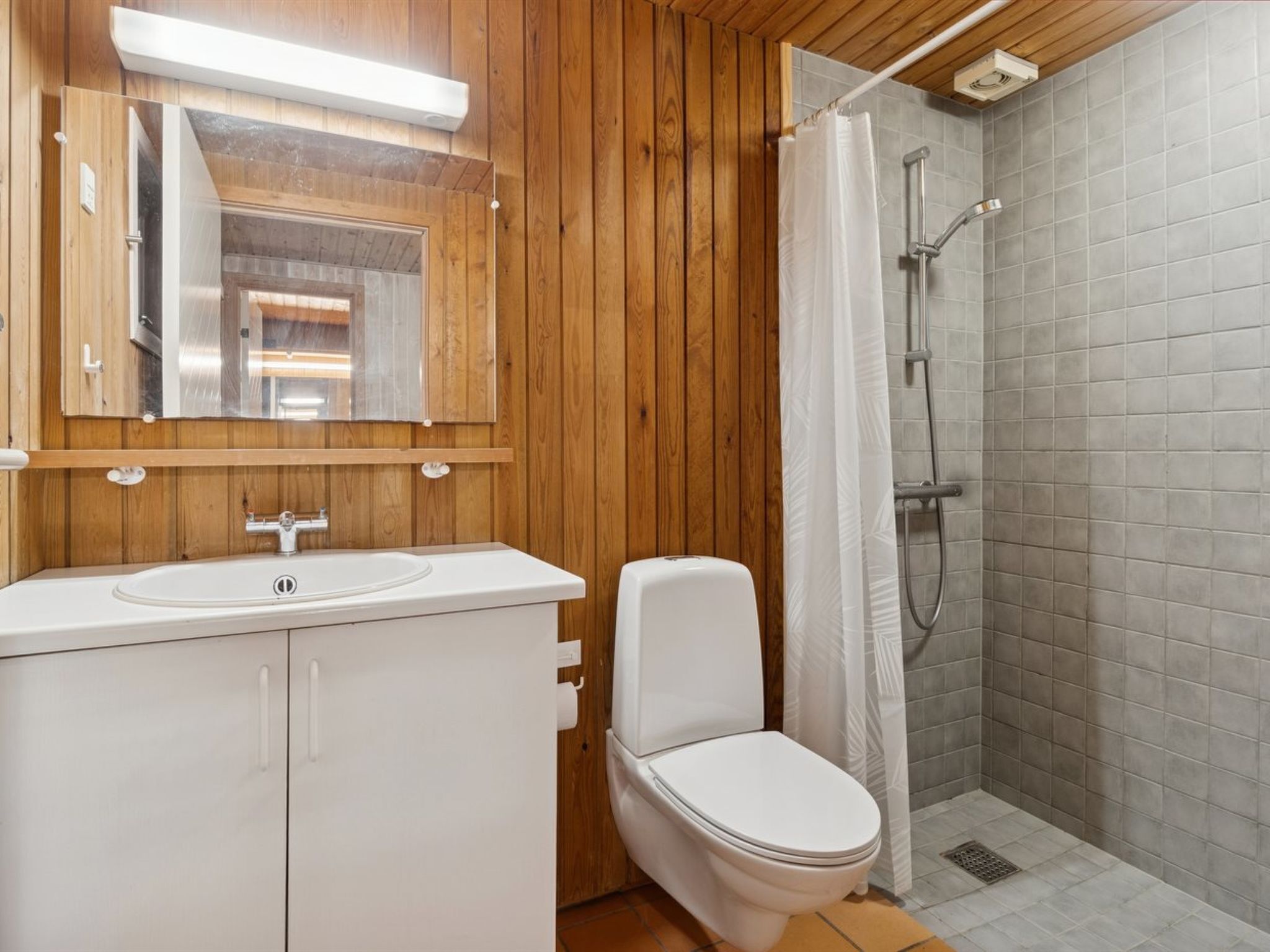 Une salle de bain avec un meuble-lavabo en bois, des toilettes, une douche avec une porte en verre et un miroir au-dessus du lavabo.