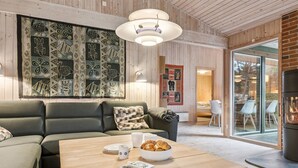 Moderni olohuone, jossa on puinen katto, vihreä sohva, puinen sohvapöytä, jonka päällä on kirja ja kulho ruokaa, sekä takka.